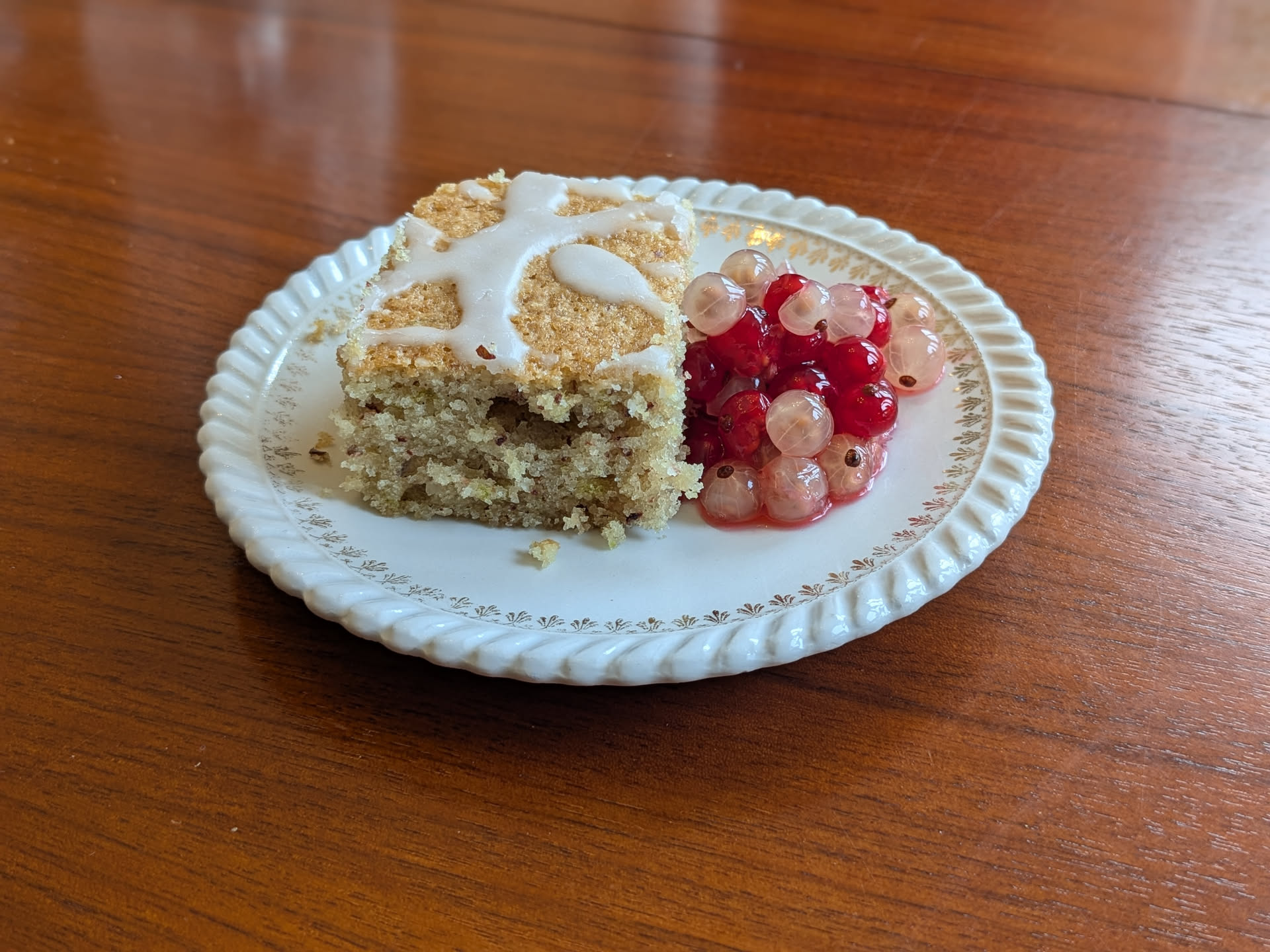 Une part de gâteau coco avec un glaçage au citron vert, accompagné de quelques groseilles blanches et rouges dans leur jus.